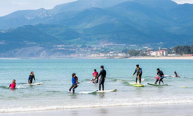 Surfistas principiantes en la playa de Hendaya con las montañas vascas al fondo